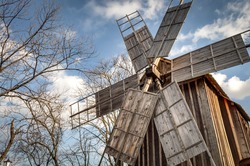 Traditional romanian windmill used by the romanians to grind grains for centuries, against a blue cloudy sky and surrounded by trees