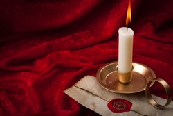 Masonic secrecy concept with a lit candle on a letter made of old vintage paper with red wax seal stamp and the freemason emblem against a scarlet color velvet background with copy space