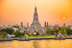 View of beautiful Temple of Dawn or Wat Arun and Thonburi west bank of Chao Phraya River at sunset with shining sun. Bangkok, Thailand