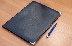 A black folder with a pen for signing documents on the table.