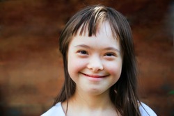 Cute smiling down syndrome girl on the brown background