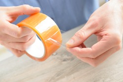 Hands with roll of transparent packaging, adhesive tape.