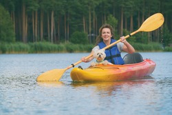 Beautiful woman is kayaking with her dog across the lake