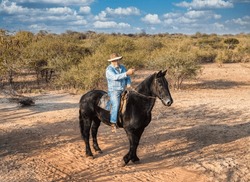 senior citizen with a beard and a cowboy hat dressed in denim, mounted on a black horse, leading the way , pointing to directions, on a horseback safari 