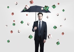 Young Business man with umbrella under gift boxes rain. On a gray background.