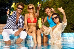 Cheerful young people sitting by swimming pool, drinking, having fun, enjoying holiday.