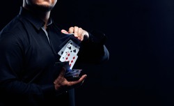 Magician illusionist showing performing card trick. Close up of hand and poker cards on black background.