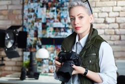 Portrait of attractive young female photographer holding camera, looking at camera.