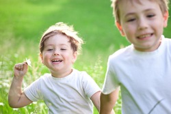 Two cute young preschool, child running and playing in green field.