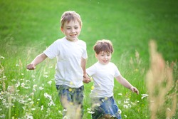 Tow cute preschool siblings holding hands and running through field of long grass.