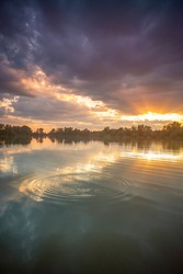 Reflection of moody and calming sunset in the lake surface with concentric circles on the background of the water during the golden hour.