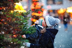 Two little kids, boy and girl having fun on traditional Christmas market during strong snowfall. Happy children enjoying traditional family market in Germany. Twins standing by illuminated xmas tree.
