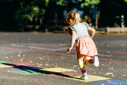 Cute little toddler girl playing hopscotch game drawn with colorful chalks on asphalt. Little active child jumping on playground outdoors on a sunny day. Summer activities for children.