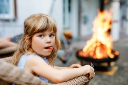 Little toddler girl girl roasting marshmallows on stick at bonfire. Child having fun at camp fire. Camping with children on backyard. Family leisure with kids at summer