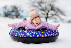 Active toddler girl sliding down the hill on snow tube. Cute little happy child having fun outdoors in winter on sledge . Healthy excited kid tubing snowy downhill, family winter time.