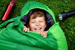 Preteen school kid boy in sleeping bag camping. Outdoors activity with children in summer. Fun and adventure camp, family and friends vacations or weekend trip. Portrait of child with flashlight.