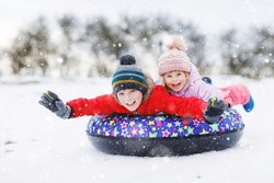 Active toddler girl and school boy sliding together down the hill on snow tube. Happy children, siblings having fun outdoors in winter on sledge. Brother and sister tubing snowy downhill, family time