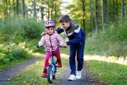 Cute little preschool girl in safety helmet riding bicycle. School kid boy, brother teaching happy healthy sister child cycling and having fun with learning bike. Active siblings family outdoors.