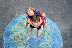 Little preschool girl and school kid boy with earth globe painting with colorful chalks on ground. Happy earth day concept. Creation of children for saving world, environment and ecology.
