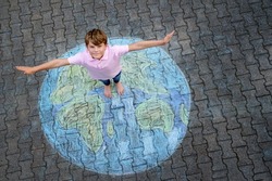 Little school boy with earth globe painting with colorful chalks on ground. Positive kid child. Happy earth day concept. Creation of children for saving world, environment and ecology.