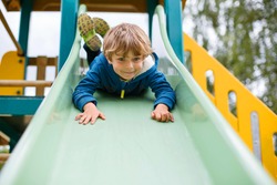 Happy blond kid boy having fun and sliding on outdoor playground. Child smiling. Summer leisure for kids.