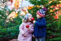 Two little smiling kids, boy and girl hugging on German Christmas market. Happy children in winter clothes with lights on background and xmas trees. Family funny brother and sister