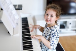 Beautiful little kid girl playing piano in living room or music school. Preschool child having fun with learning to play music instrument. Education, skills concept.