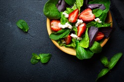 Healthy vegetable salad with strawberry and cheese in wooden bowl on a dark background