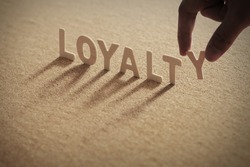 LOYALTY wood word on compressed board with human's finger at Y letter