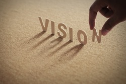 VISION wood word on compressed board with human's finger at N letter
