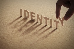 IDENTITY wood word on compressed board with human's finger at Y letter