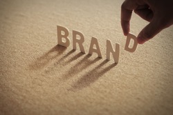 BRAND wood word on compressed or corkboard with human's finger at D letter.
