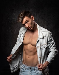 European athletic young man, posing without outerwear, in sports physical form. On a dark textured background. Jacket on the shoulder.