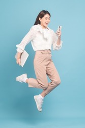 Young beautiful asian woman with smart casual cloth use smartphone and jump isolated on blue background