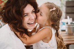 Portrait of little daughter kissing her beautiful happy mother