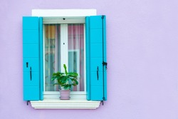 Window with blue shutters on the violet wall. Colorful architecture in Burano island, Venice, Italy.