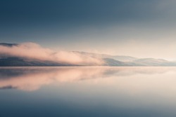 Beautiful lake in misty morning. Mountains and clouds are reflected in the calm water surface. Autumn landscape. South Ural, Russia.