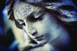 Death concept. Close Up of ancient statue of crying angel with tears in face as symbol of end of human life. Selective focus on eyes.