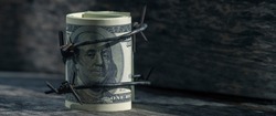 Economic warfare, sanctions and embargo busting concept. Close up US Dollar money wrapped in barbed wire. Horizontal image.