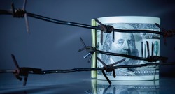 Economic warfare and sanctions. US Dollar bills money wrapped in barbed wire. Horizontal image.
