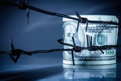 Economic warfare and sanctions. US Dollar bills money wrapped in barbed wire. Horizontal image. Copy space for text or design.