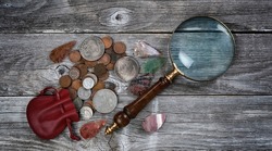 Collection of United States rare coins and Native American arrowheads with antique magnifying glass on rustic wood background 