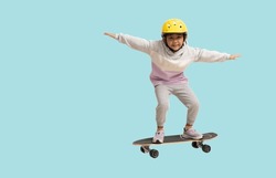 Happy asian smiling little girl playing skateboard wearing a helmet, Full body portrait isolated on pastel plain light blue background
