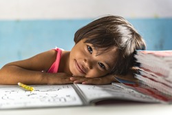 a very young girl student in the school has her head on the exercise book and smiling friendly. Thai school in a small village