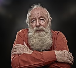 Old age concept. Portrait of an old man with white beard sadly looking at camera. Black background. 