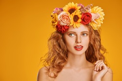 Portrait of a beautiful young woman with long curly red hair and in a wreath of flowers on a yellow background. Autumn beauty. Make-up and cosmetics.