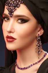 Arabian beauty, fashion. Close-up portrait of a beautiful oriental woman with traditional make-up, black hijab and jewelry on a black background. Make-up and cosmetics. 