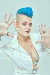 Portrait of a cool girl punk rock musician with bright makeup and blue mohawk posing at studio expressively. Youth alternative culture. White background.