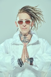 Portrait of a modern punk rock musician with dreadlocks posing in white suit and white sunglasses on a light background. Youth alternative culture. Futuristic space and cybepunk style. 