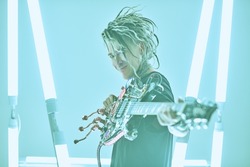 Modern punk rock music. Portrait of an expressive punk rock musician with dreadlocks posing with an electric guitar among neon lamps. Youth alternative culture. Cyberpunk and space style.